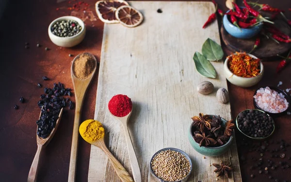 Varias especias indias en cucharas de madera, semillas, hierbas y nueces y tablero de madera vacío —  Fotos de Stock