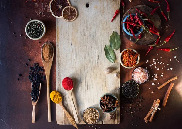 Varias especias indias en cucharas de madera, semillas, hierbas y nueces y tablero de madera vacío —  Fotos de Stock