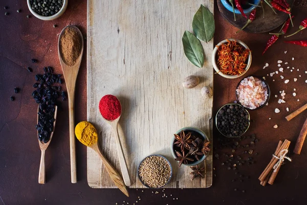 Various indian spices in wooden spoons, seeds, herbs and nuts and empty wooden board — Stock Photo, Image
