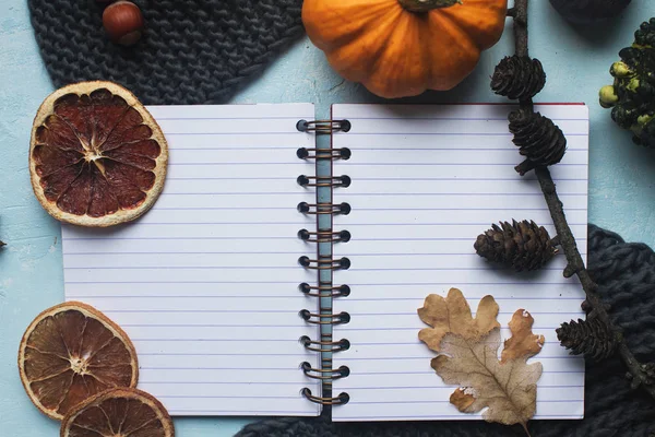 Cozy autumn background, notebook, decorative pumpkins, dried oranges, candle, nuts, cinnamon and autumn leaves