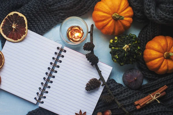 Cozy autumn background, notebook, decorative pumpkins, dried oranges, candle, nuts, cinnamon and autumn leaves