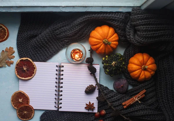 Cozy autumn background, notebook, decorative pumpkins, dried oranges, candle, nuts, cinnamon and autumn leaves