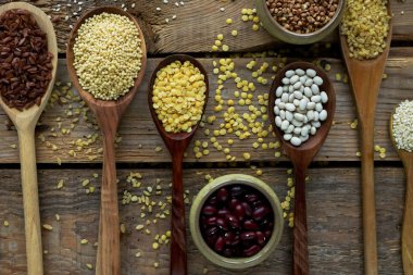 Ham organik tahıl tahıllar, tohum ve fasulye rustik ahşap zemin üzerine tahta kaşıklar