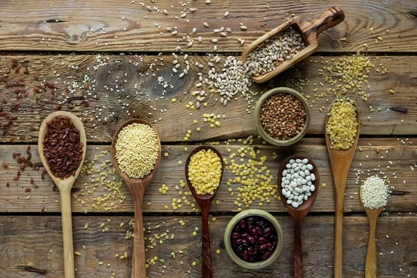 Raw organic cereal grains, seeds and beans in wooden spoons on rustic wooden background — Stock Image Raw organic cereal grains, seeds and beans in wooden spoons on rustic wooden background Royalty Free Stock Photos