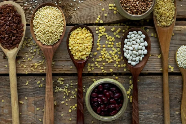 Raw organic cereal grains, seeds and beans in wooden spoons on rustic wooden background — Stock Image Raw organic cereal grains, seeds and beans in wooden spoons on rustic wooden background Royalty Free Stock Photos