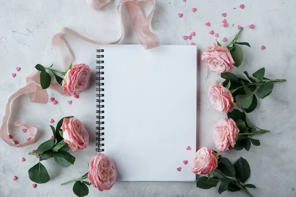 Defter, gül, pembe kurdele ve beyaz arka plan üzerinde kalp şeklinde tatlı şekerler