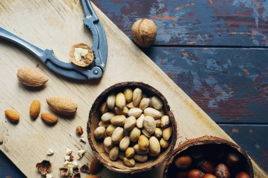 Hindistan cevizi kaselerinde fındık karışımı ve koyu ahşap masa üzerinde klasik kesim tahtası, ceviz, badem, fındık, kaju, sağlıklı çeşitli süper yiyecekler, üst görünüm, seçici odaklanma.