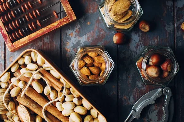 Mix of nuts in boxes, bowls and glass jars on dark wooden table, walnuts, almond, hazelnut, cashew, healthy various superfoods, top view, selecitve focus