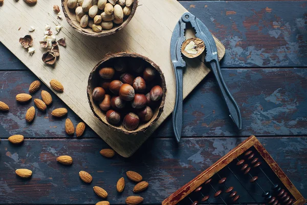 Mix of nuts in coconut bowls and vintage cutting board on dark wooden table, walnuts, almond, hazelnut, cashew, healthy various superfoods, top view, selecitve focus