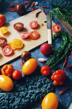 Koyu taş masa ve eski ahşap tahta, sağlıklı yaşam tarzı, organik gıda konsepti ve seçici odaklanma üzerine renkli çiğ domates ve otların karışımı.