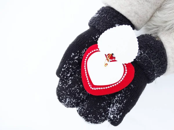 Manos de mujer en manoplas con corazón rojo en la nieve — Foto de Stock