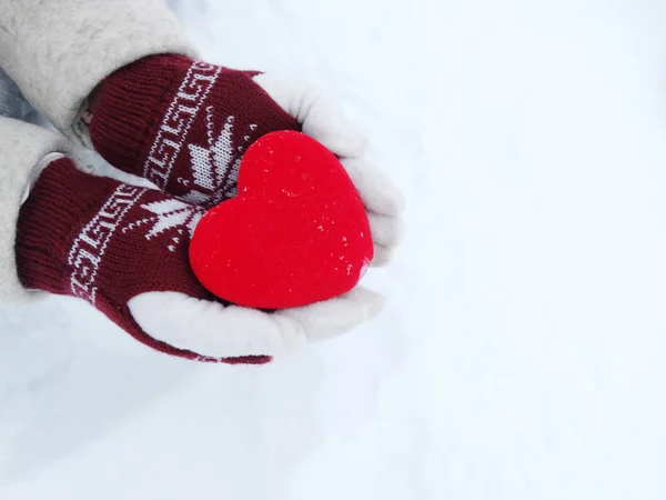 Manos de mujer en manoplas con corazón rojo en la nieve — Foto de Stock