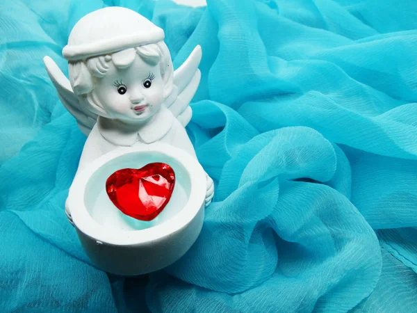 angel toy holding crystal heart in hands on silky background
