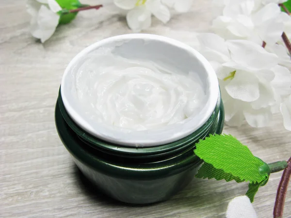 Cosmetic cream for face care and white sakura flowers — Stock Photo, Image