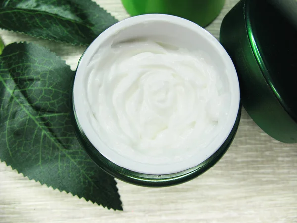 Crema cosmetica per la cura del viso e foglie verdi — Foto Stock