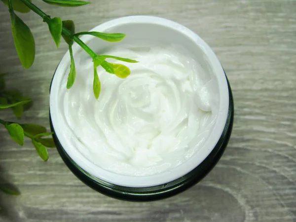 Crema cosmética para el cuidado de la cara y hojas verdes — Foto de Stock