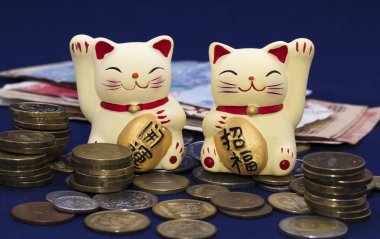 Two lucky cats (Maneki-Neko) among metal coins and paper banknotes. Inscriptions on the tablets 