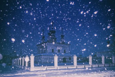 Bir kar yağışı sırasında eski bir beyaz kilise ile kış gece manzarası. Suzdal, Rusya. Büyük kar taneleri hareket bulanıklığı, parlama. Vintage Klasik kamera filtre.