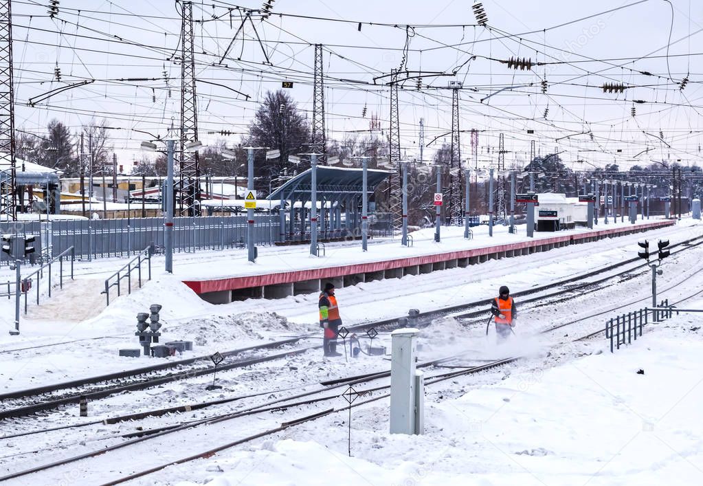 Railway workers in uniform  clean snow from railway tracks using a jet of compressed air.