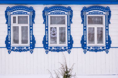 Beyaz cephe ahşap bir ev. Üç windows dekoratif mavi ahşap oyma kare ile. Frost üstünde pencere eşiği. Rus halk tarzı. Önden Görünümü Kapat.