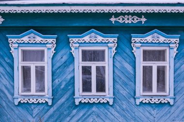 Mavi boyalı cephe ahşap bir ev. Üç windows mavi ve beyaz dekoratif ahşap kare oyma ile. Frost üstünde pencere eşiği. Rus Halk tarzı. Önden Görünümü Kapat.