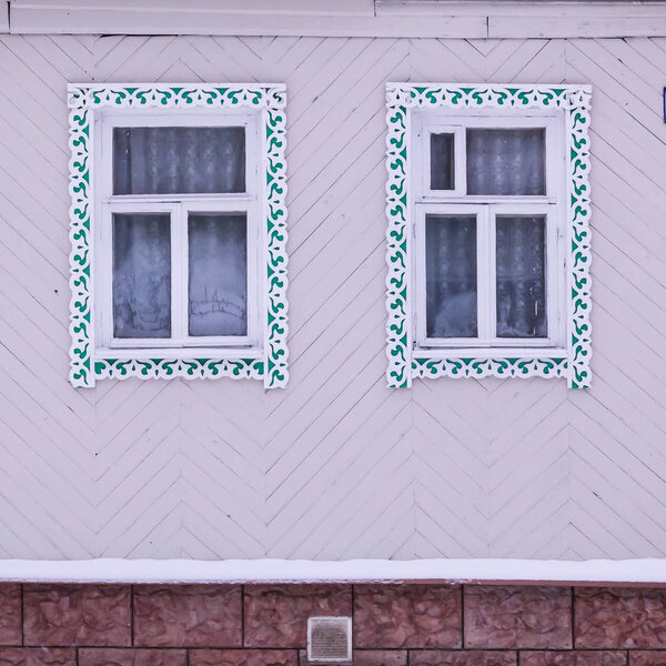 Pink facade of a wooden house. Two windows with white and green decorative wood carving frame. Frost on windows. Russian folk style. Front view close up.