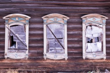 Terk edilmiş bir ahşap evin duvarına günlük. Kırık camlar, cam yerine kontrplak. Üç windows dekoratif ahşap oyma kare ile. Rus halk tarzı. Önden Görünümü Kapat.