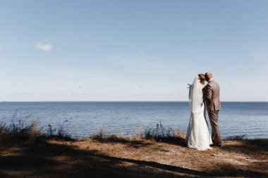 Gelin ve damat denizin kenarında durup manzarayı izliyorlar.