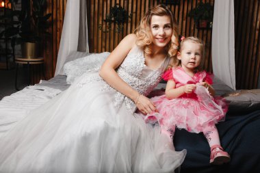 Anne ve kızı gece elbisesi içinde lüks bir yatakta oturuyorlar.