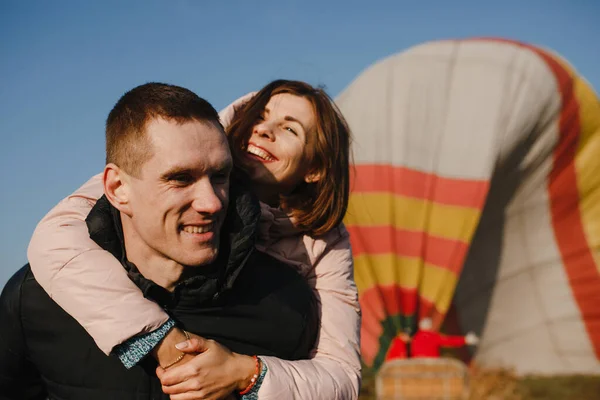 Hombre feliz con mujer sonriente en su espalda en el fondo del globo aerostático —  Fotos de Stock