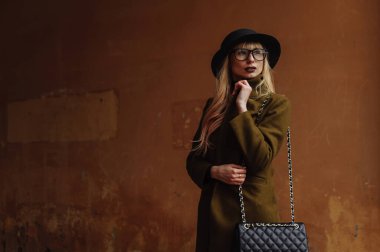 Gözlüklü ve siyah şapkalı bir kadın duvarın arkasına bakıyor. Kadın portresi