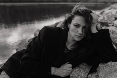 Nehrin yanındaki taşların üzerinde yatan paltolu kadın. Kadın portresi