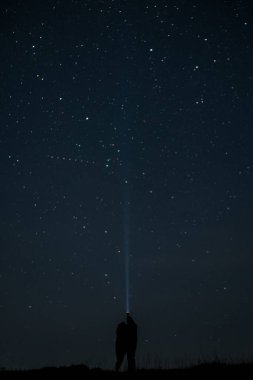 Yıldızlı gökyüzünün altında el feneri yukarıya doğru tutulmuş birbirine aşık bir çift. Aşk hikayesi.