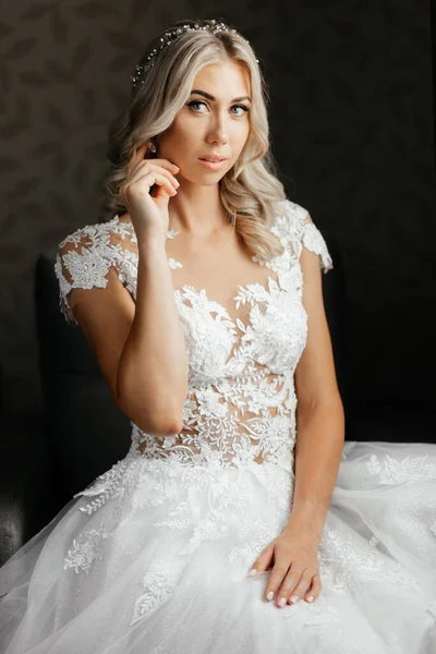 Beautiful bride in the wedding dress sitting and touching her earrings — Stock Photo, Image