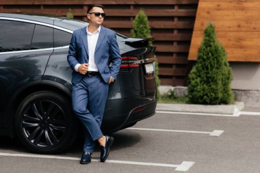 Arabanın yanında duran takım elbiseli şık adam.