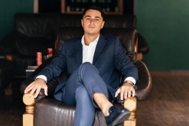 Beyaz gömlekli ve takım elbiseli ciddi bir adam koltukta oturuyor.