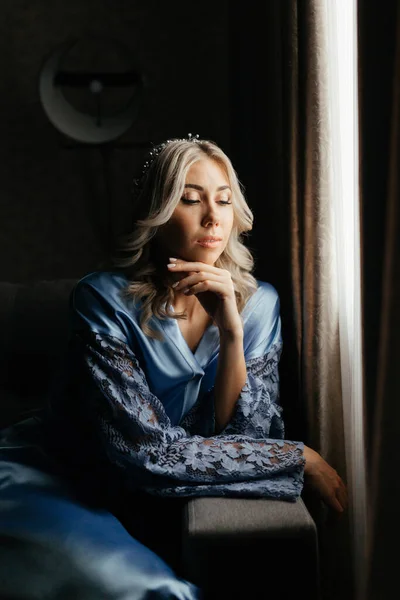 Γυναίκα στο μπλε peignoir κάθεται μπροστά από το παράθυρο και κοιτάζει κάτω — Φωτογραφία Αρχείου