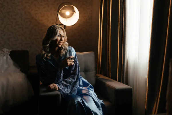 Ξανθιά γυναίκα στο μπλε peignoir με ένα ποτήρι σαμπάνια στα χέρια της — Φωτογραφία Αρχείου
