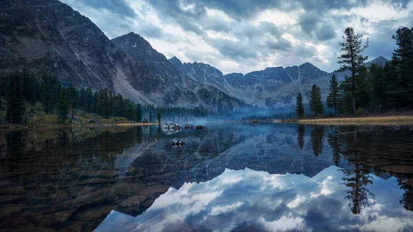 Lake with reflection of clouds among the mountains at sunset in the forest