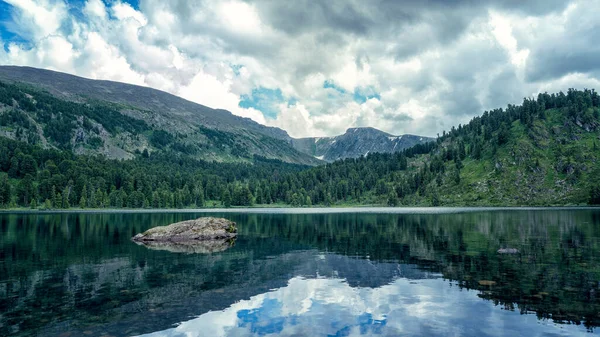 Large Karakol lake in the mountains, the reflection of mountains and clouds in the lake