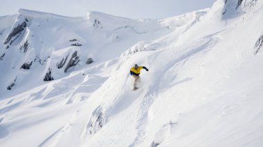 Kar kayaklarından atlayan bir snowboardcu dağ yolundan aşağı iniyor.
