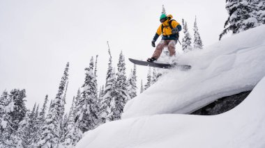 Bir snowboardcu kışın karda bir uçurumdan atlıyor.