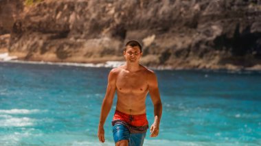 The guy goes against the blue of the ocean in shorts