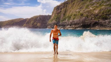 The guy is running away from the waves of the ocean in shorts on the beach sun heat