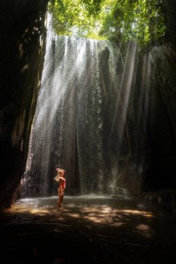 Girl in swimsuit on waterfall Tukad Cepung ray from the sun of Bali