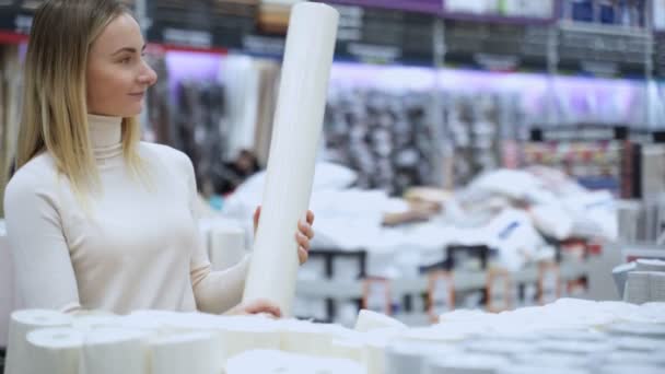 Menina escolhe papel de parede na loja de construção. Mulher seleciona papel de parede nas prateleiras da loja . — Vídeo de Stock