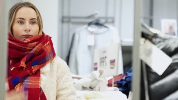 Zimowe zakupy kobieta próbuje na szalik patrząc w lustro uśmiechnięty szczęśliwy gospodarstwa wewnątrz w sklepie odzieżowym. — Wideo stockowe