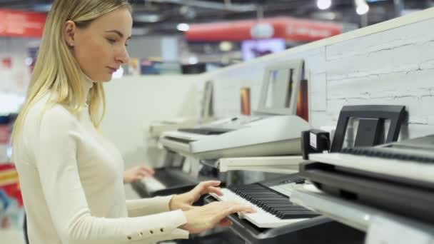 Smiling positive girl choosing synthesizer in music instruments shop — Stock Video