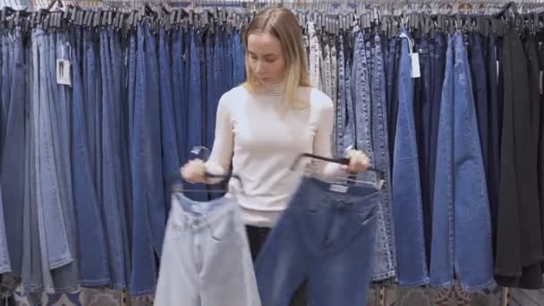 Smiling girl shopper choosing new jeans at store — Stock Video