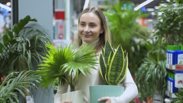 Kobieta wchodzi do sklepu, trzymając dwa doniczki roślin.. — Wideo stockowe